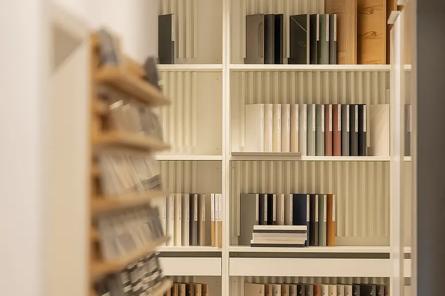 Weißes maßgefertigtes Regalsystem mit ordentlich sortierten Materialmustern im hellen Ausstellungsraum des Küchenhauses und Schreinerei Kleinbach.